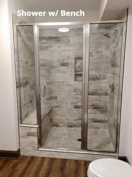 Walk-in shower with glass doors and built-in bench in a tiled bathroom.