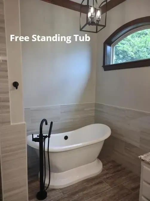 Bathroom with a white freestanding tub, black faucet, beige tile, and arched window