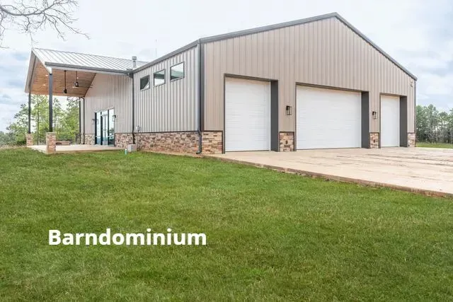 Modern gray barndominium with stone base, white garage doors, and large grassy lawn