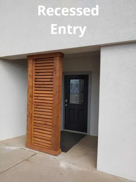 Recessed entry with white walls, a black door, and a wooden louvered screen beside the doorway