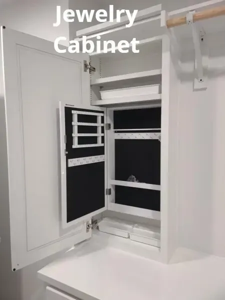 Open white jewelry cabinet with black-lined drawers and compartments on a wall