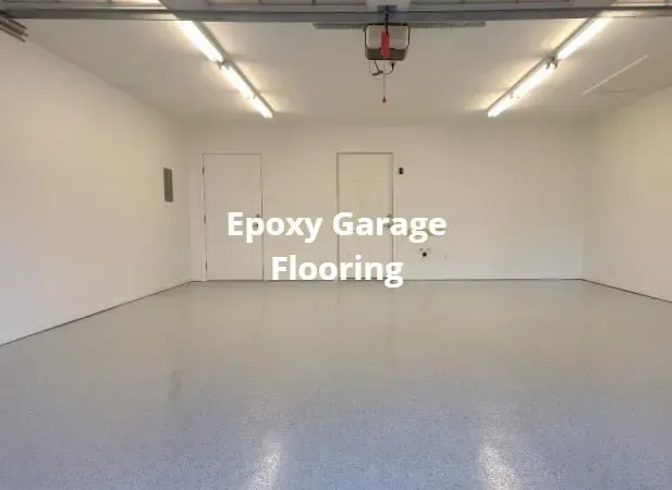 Empty garage with smooth light gray epoxy flooring and white walls, labeled “Epoxy Garage Flooring”