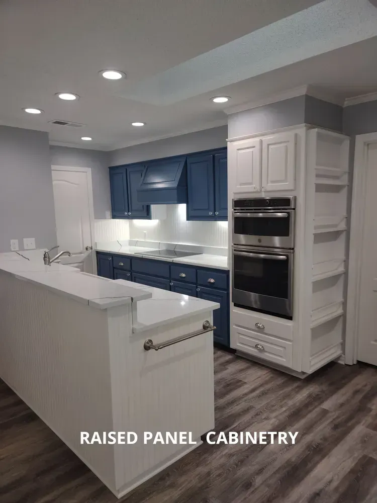 Bright white kitchen with blue raised-panel cabinets, built-in oven, and recessed ceiling lights