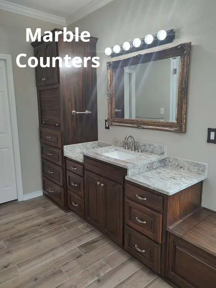 Bathroom vanity with marble countertops, wood cabinets, and a large mirror with lights