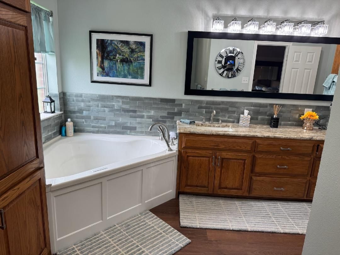 Bathroom with white tub, wood vanity, gray tile, and large mirror with lights