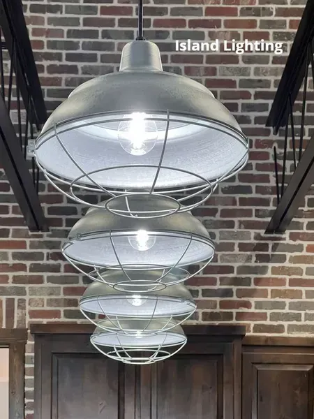 Four stacked silver industrial pendant lights hanging against a brick wall and wood doors.