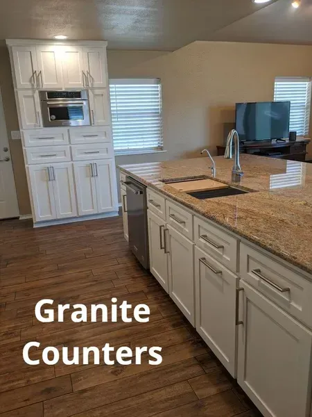 Kitchen with white cabinets, granite island counters, and a stainless sink in a bright open room