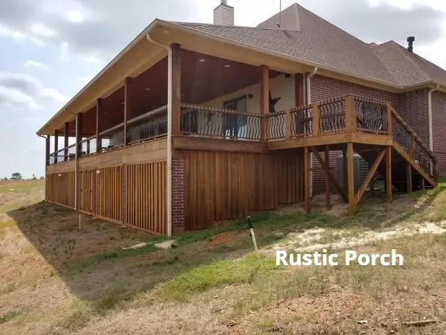 Large rustic wooden porch with railings and stairs on a house, overlooking a grassy yard.