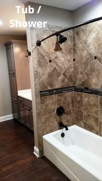 Bathroom tub-shower with beige tile, glass door, and white tub beside a vanity.