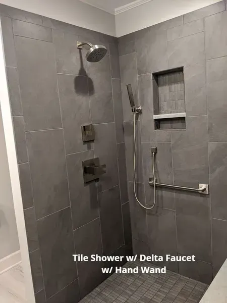 Gray-tiled walk-in shower with Delta fixtures, handheld wand, and recessed niche on the right.
