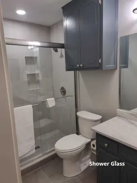 Modern bathroom with glass shower, toilet, vanity, and navy wall cabinet