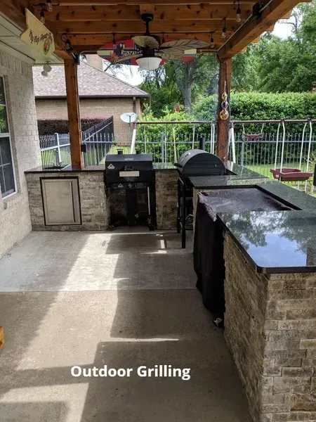 Covered outdoor grilling area with built-in stone counters and a black grill on a patio