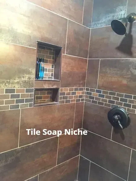 Shower corner with built-in tile soap niche and brown tiled walls, showing shower fixtures and mosaic accent strip