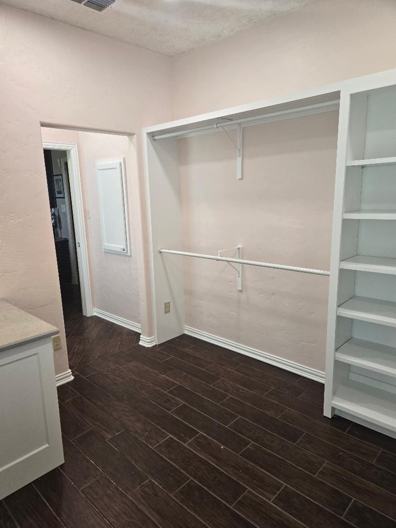 Walk-in closet with white shelving, hanging rods, and dark wood floors in a light pink room