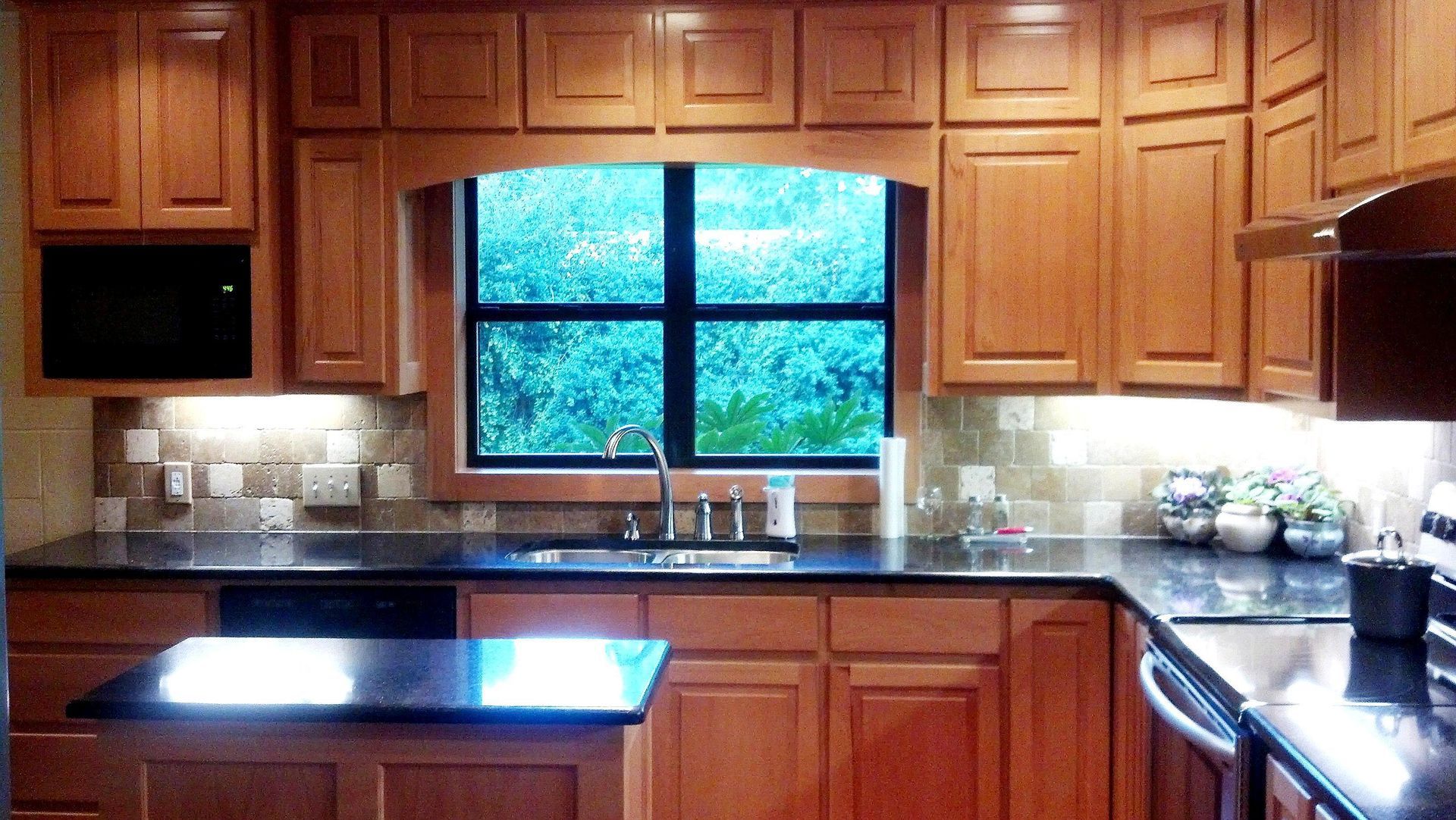 Wooden kitchen with a center island, black countertops, and a window above the sink.