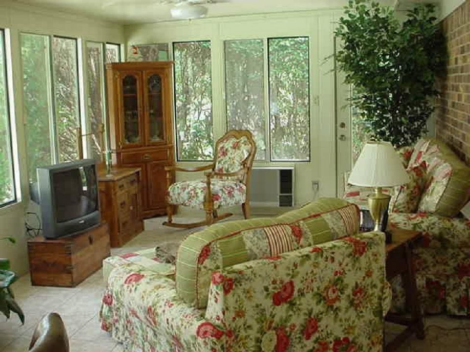 Floral-upholstered living room with sofa, armchair, TV, cabinet, and large windows overlooking greenery