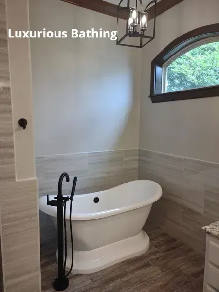 Luxurious bathroom with freestanding tub, handheld shower, and arched window