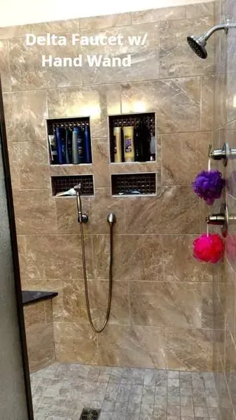 Bathroom shower with Delta faucet, handheld wand, beige tile, and two recessed shelves.