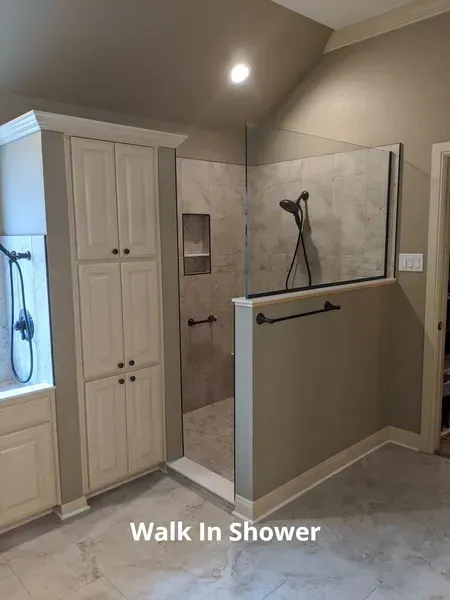 Walk-in shower with glass partition, beige tile, built-in cabinet, and towel bar in a bathroom.