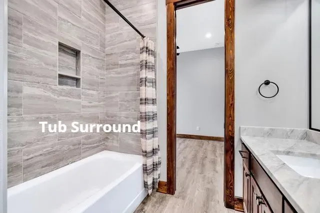 Bathroom with white tub surround, striped shower curtain, and vanity beside wood flooring.