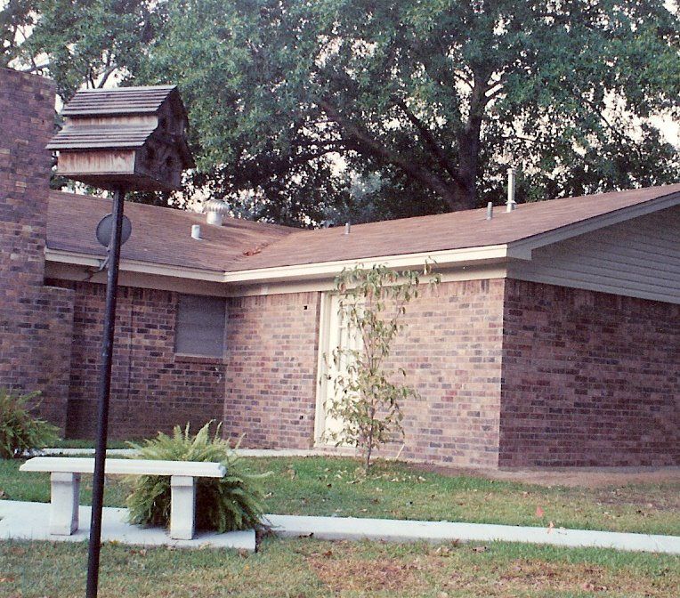 Brick building with a sloped roof, a lamp post, and a bench in a grassy yard.