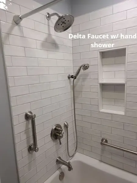 White-tiled shower with grab bars, tub, and Delta handheld showerhead in a bathroom