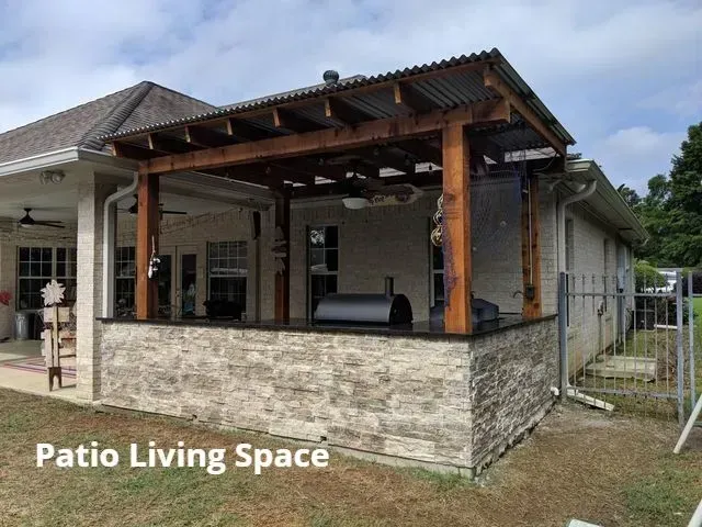 Covered patio living space with stone half-wall and wooden beams attached to a house