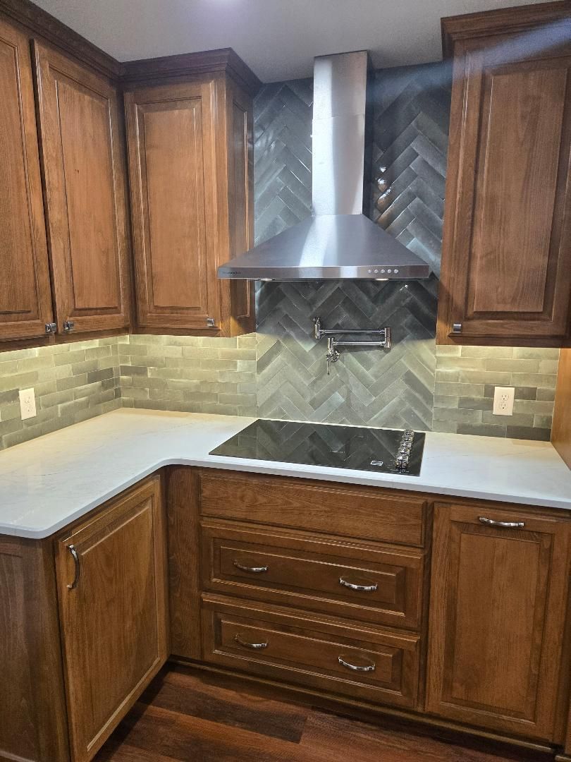 Wood kitchen corner with white countertops, dark cabinets, stainless range hood, and black cooktop