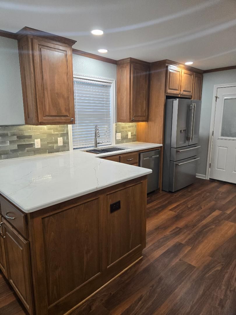 Modern kitchen with wood cabinets, white countertops, dark hardwood floor, and stainless steel refrigerator