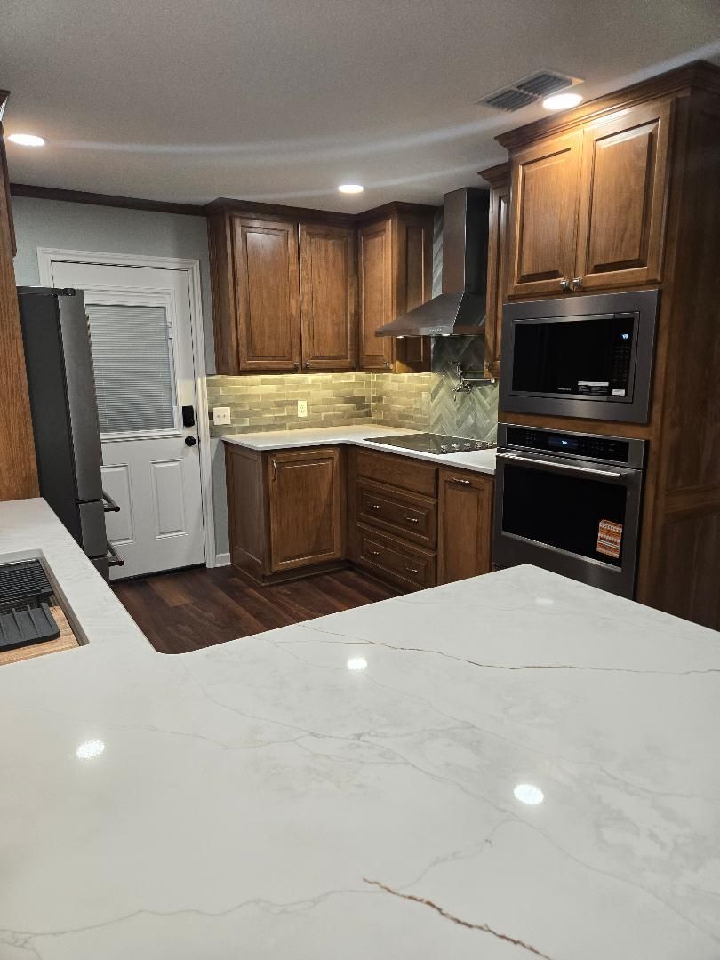 Modern kitchen with wood cabinets, white quartz island, built-in oven, and stainless range hood.
