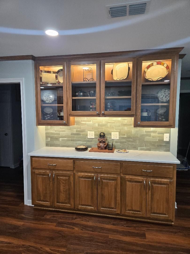 Built-in wooden cabinets with glass doors above a white countertop in a home interior.