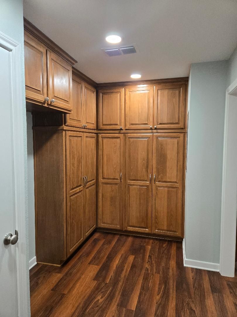Small pantry with wood cabinets, dark hardwood floor, and ceiling lights in a narrow hallway.