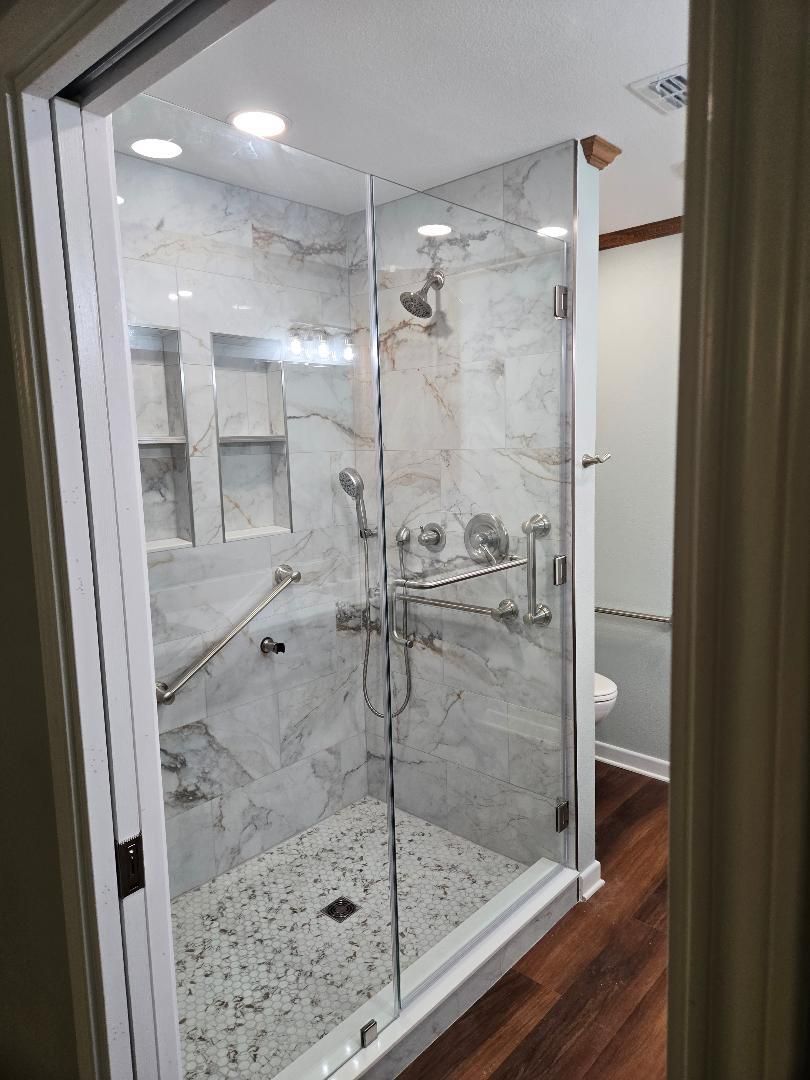 Modern marble walk-in shower with glass doors, chrome fixtures, and a built-in shelf in a bathroom.