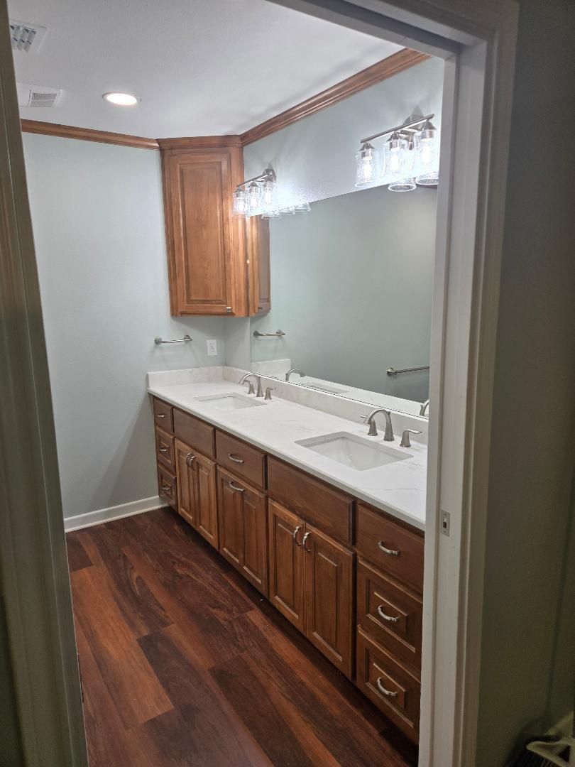 Bathroom vanity with wood cabinets, white countertops, and large mirror under window trim
