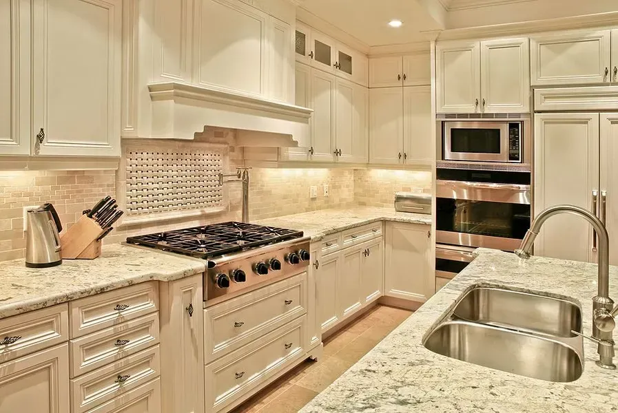 Bright cream-colored modern kitchen with granite counters, white cabinets, and stainless steel appliances
