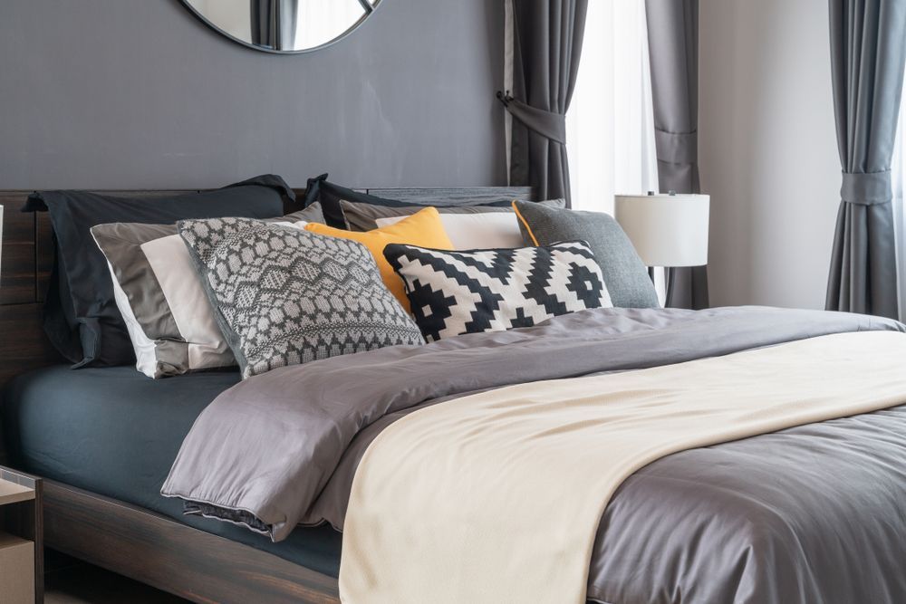 Modern bedroom with a neatly made bed, gray walls, patterned pillows, and soft natural light
