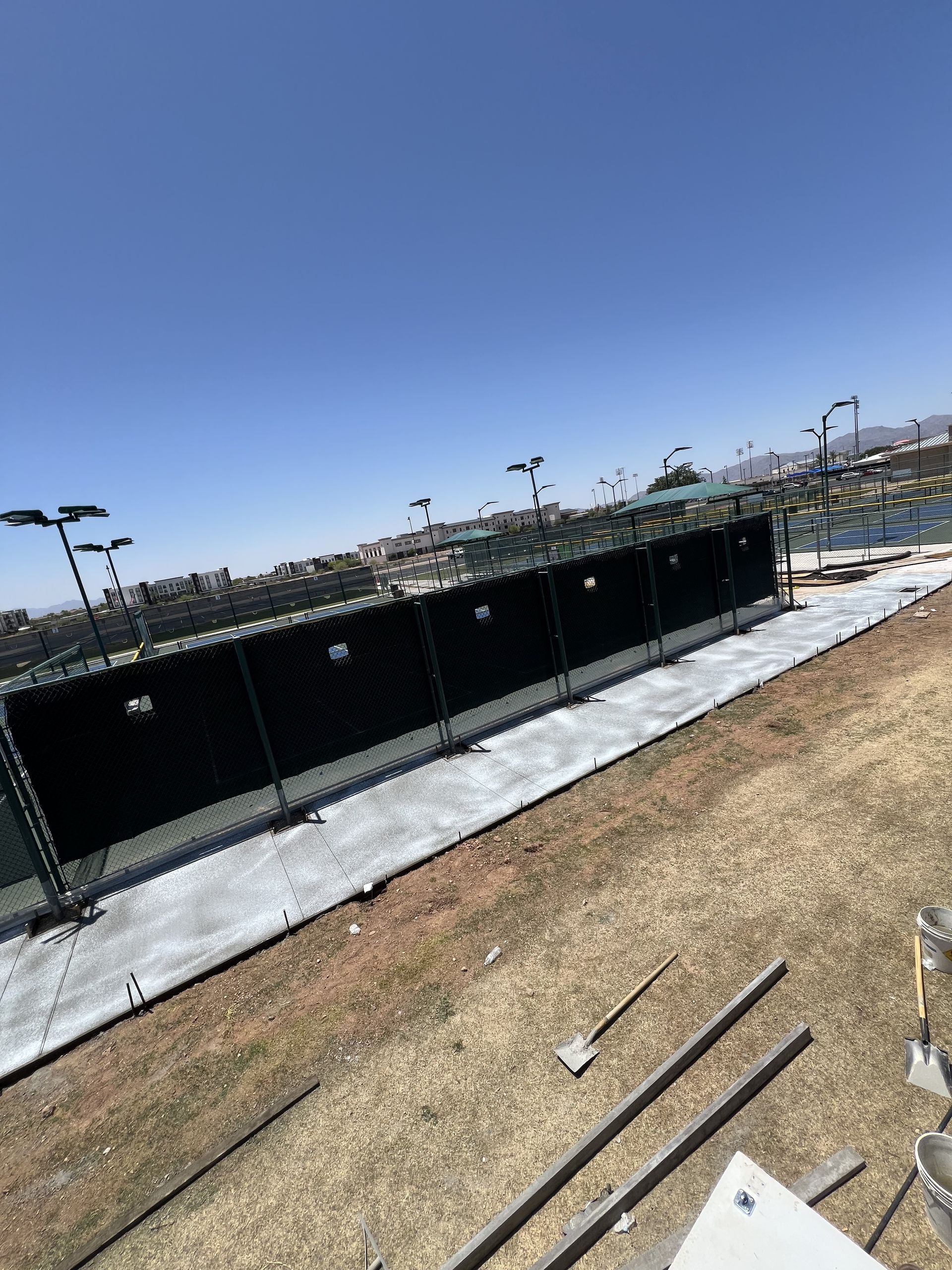 Outdoor construction site with a black fence around a concrete area under a clear blue sky