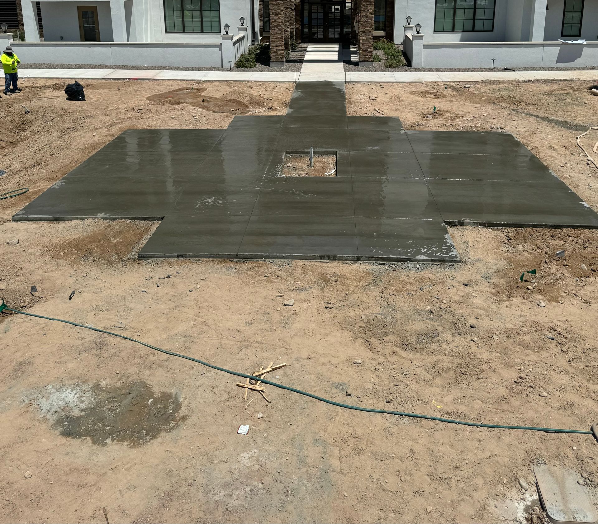 Freshly poured concrete slab on a dirt construction site in front of a house