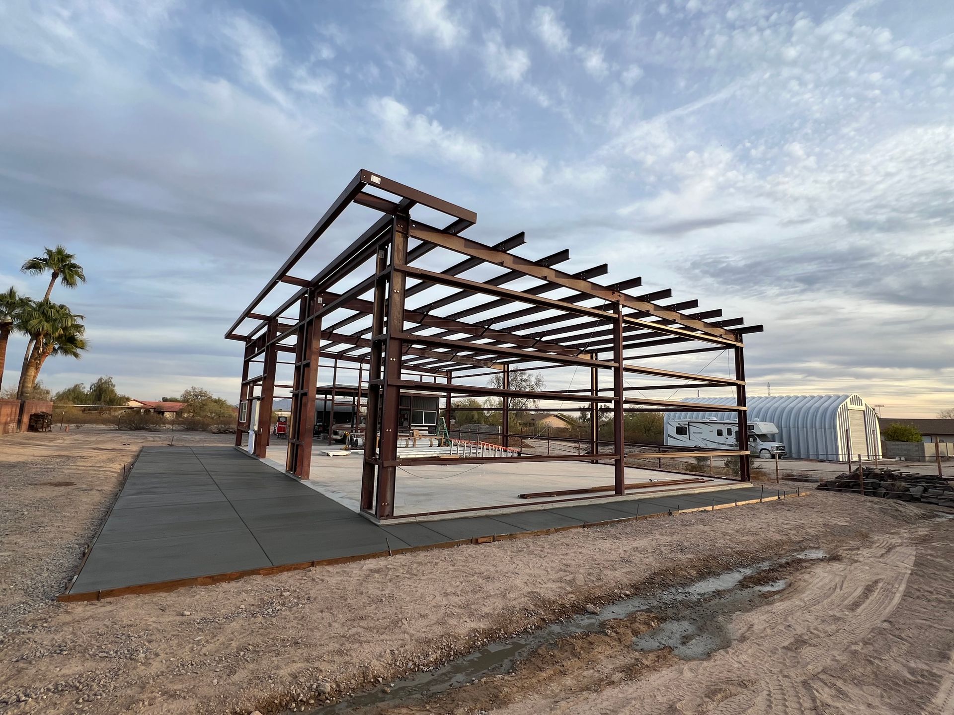 Rusty steel frame of a building under construction beside a gravel road in a desert lot
