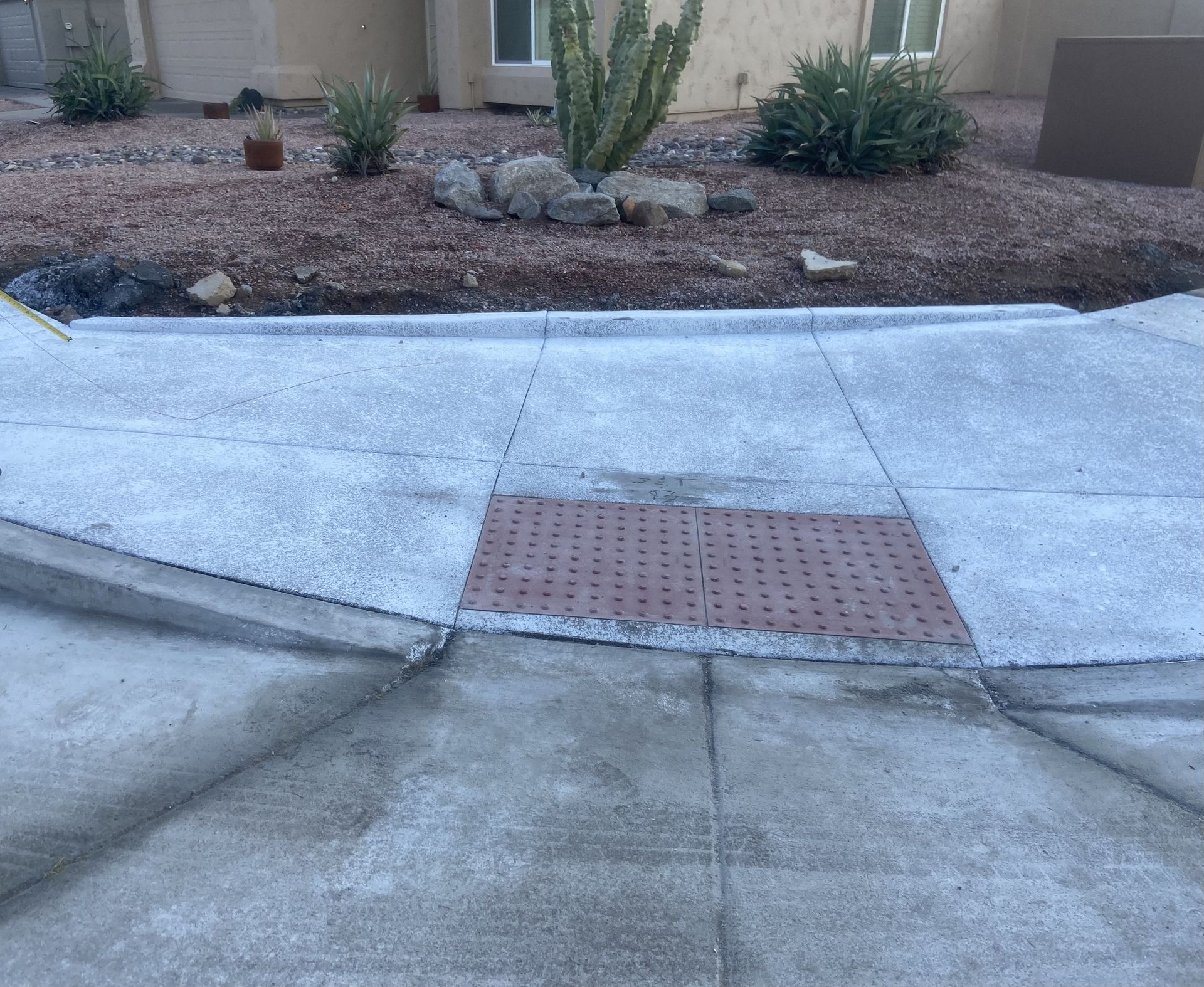 Concrete sidewalk with a red tactile paving panel and a landscaped desert yard in front of a house.
