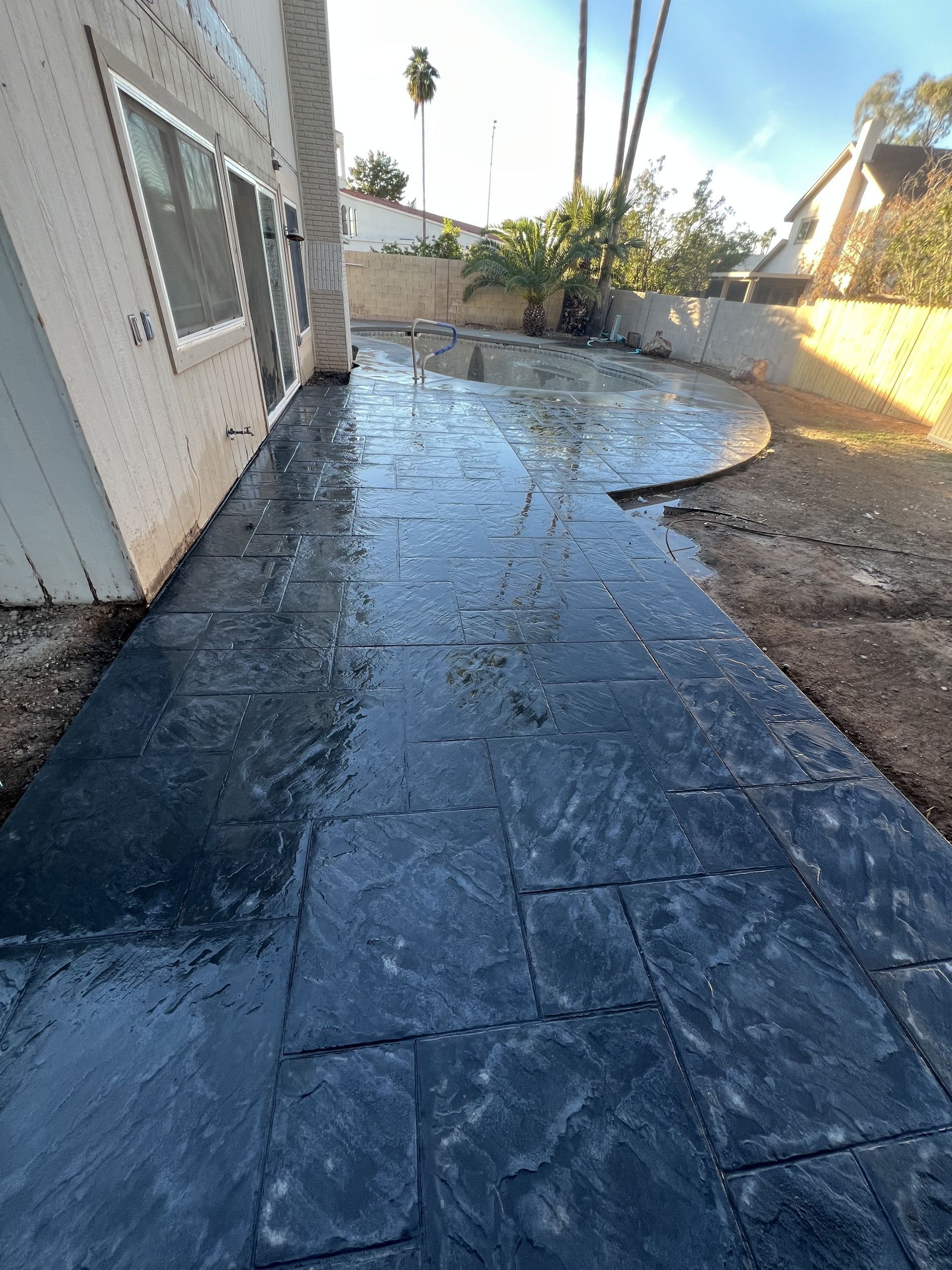 Wet concrete walkway beside a house, reflecting sunlight with a partially broken edge.