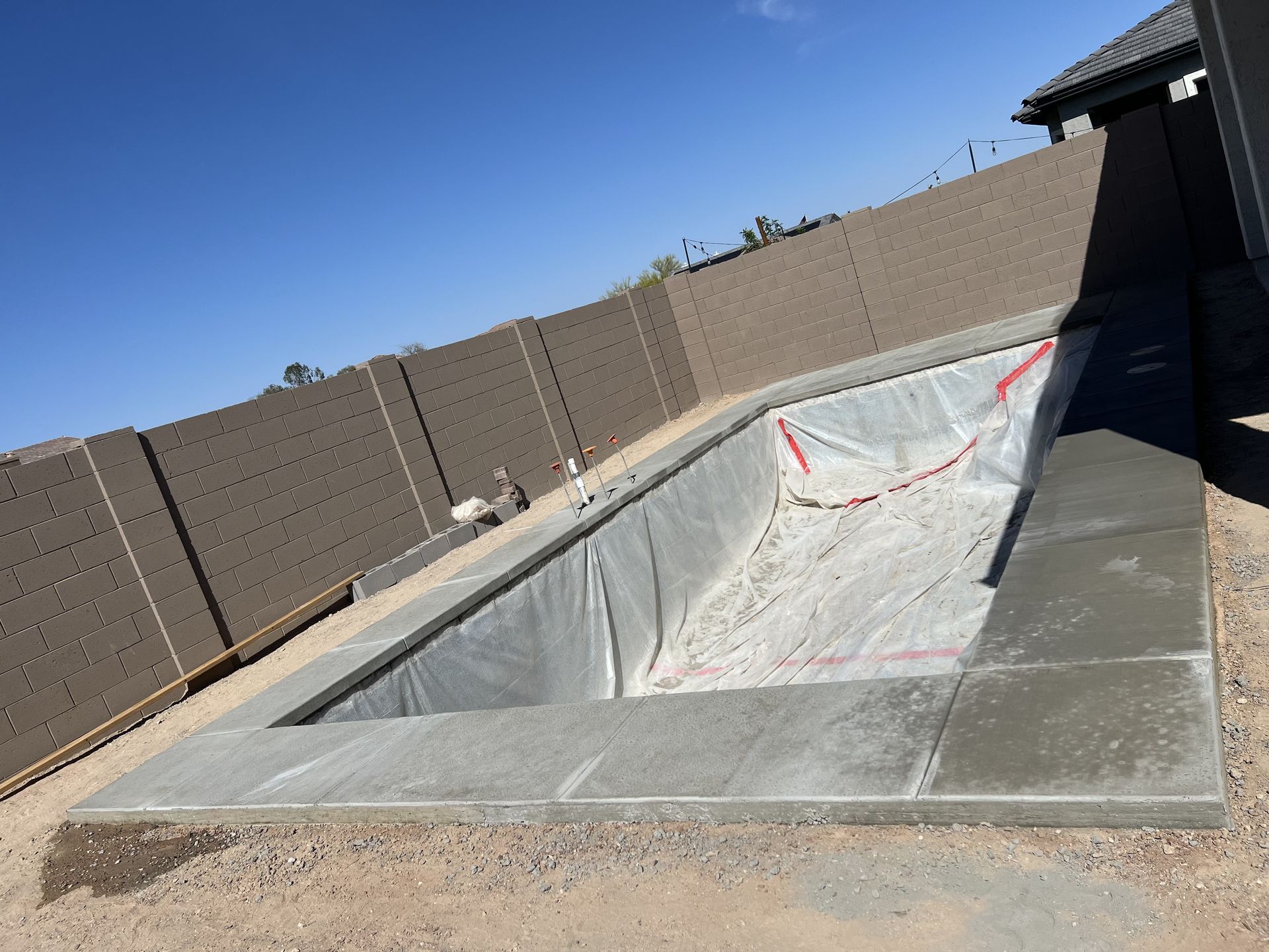 Empty backyard swimming pool under construction with concrete deck and temporary fencing