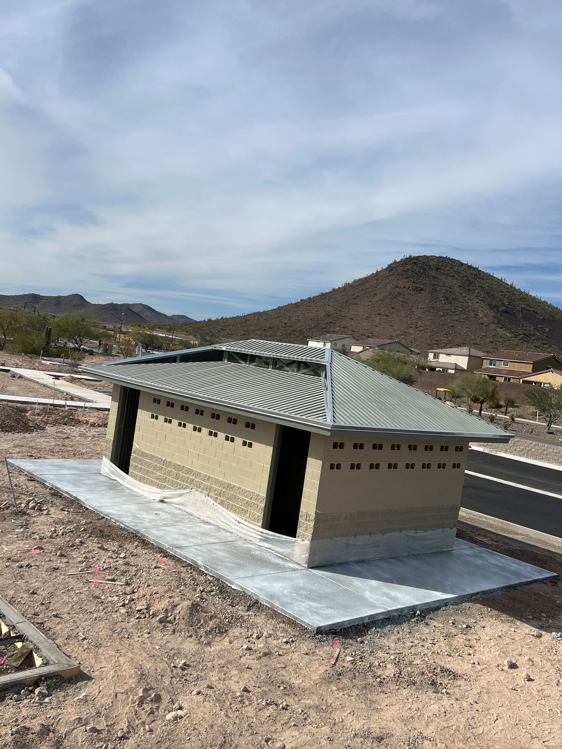 Small tan utility building with green roof beside a road in a desert landscape
