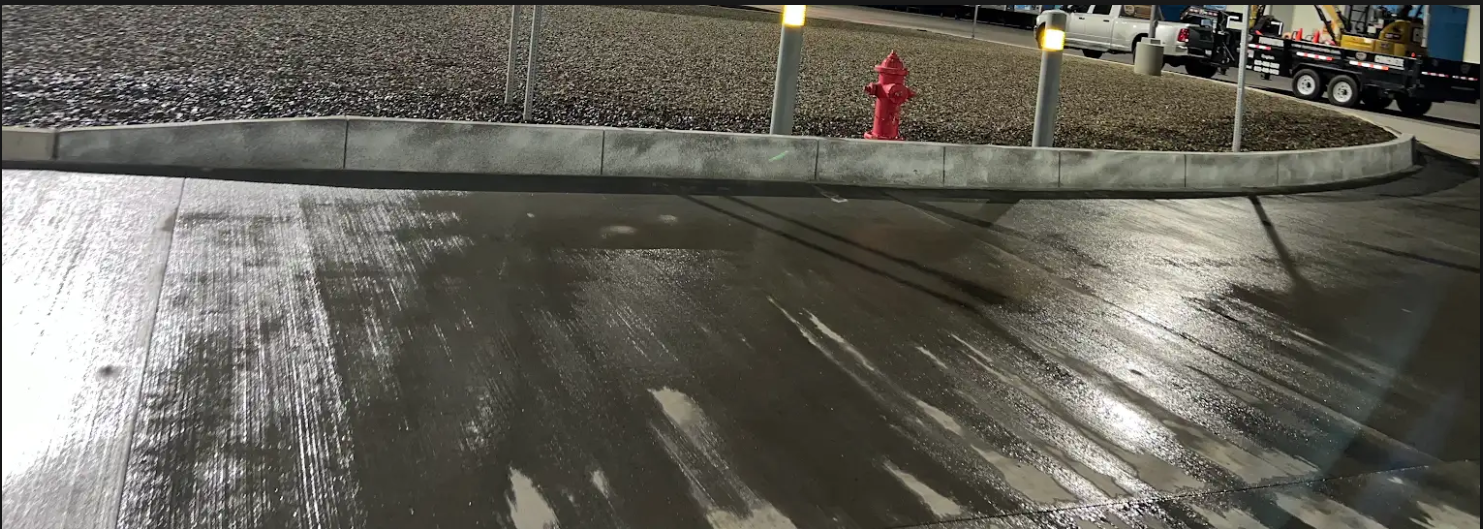 Snow-dusted curb and wet pavement at night, with a person in a red coat by the road edge.