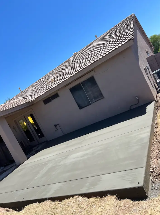 Tilted view of a house with a large concrete driveway and tiled roof under bright sunlight