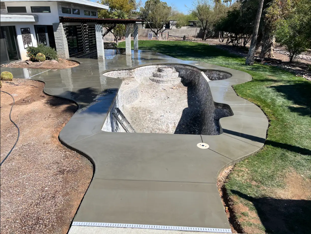 Drying concrete around a large rock feature in a backyard with a house and grass nearby