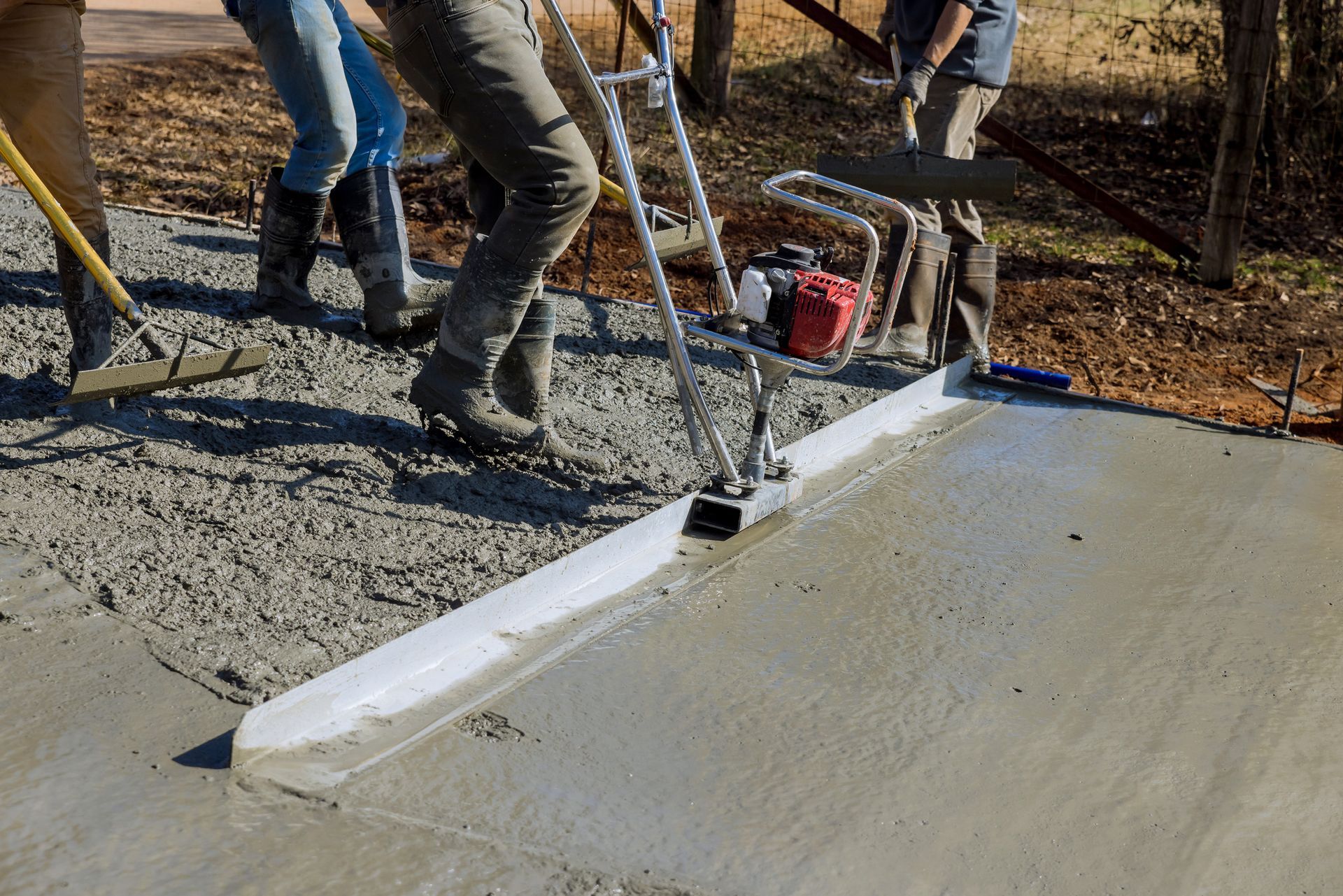 Construction workers leveling and screeding freshly poured concrete slab.