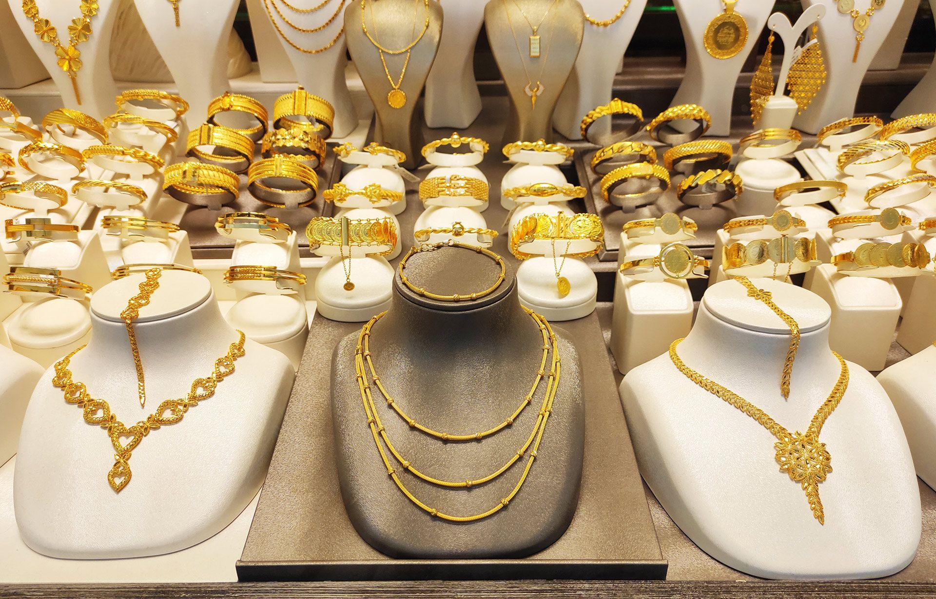 Gold necklaces and bracelets displayed on white busts in a jewelry shop window