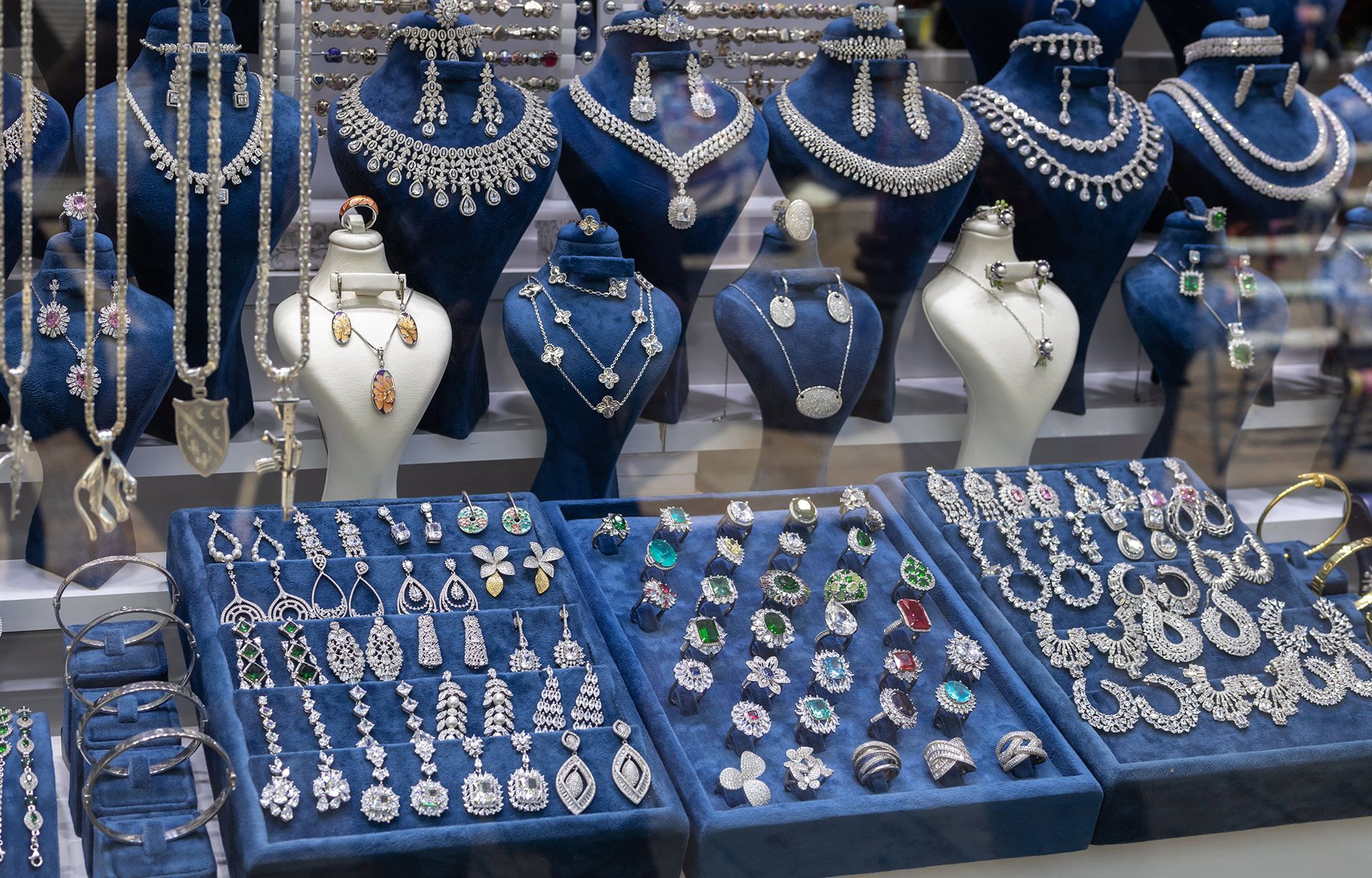 Jewelry display with blue trays, necklaces, bracelets, rings, and white mannequin busts in a shop window