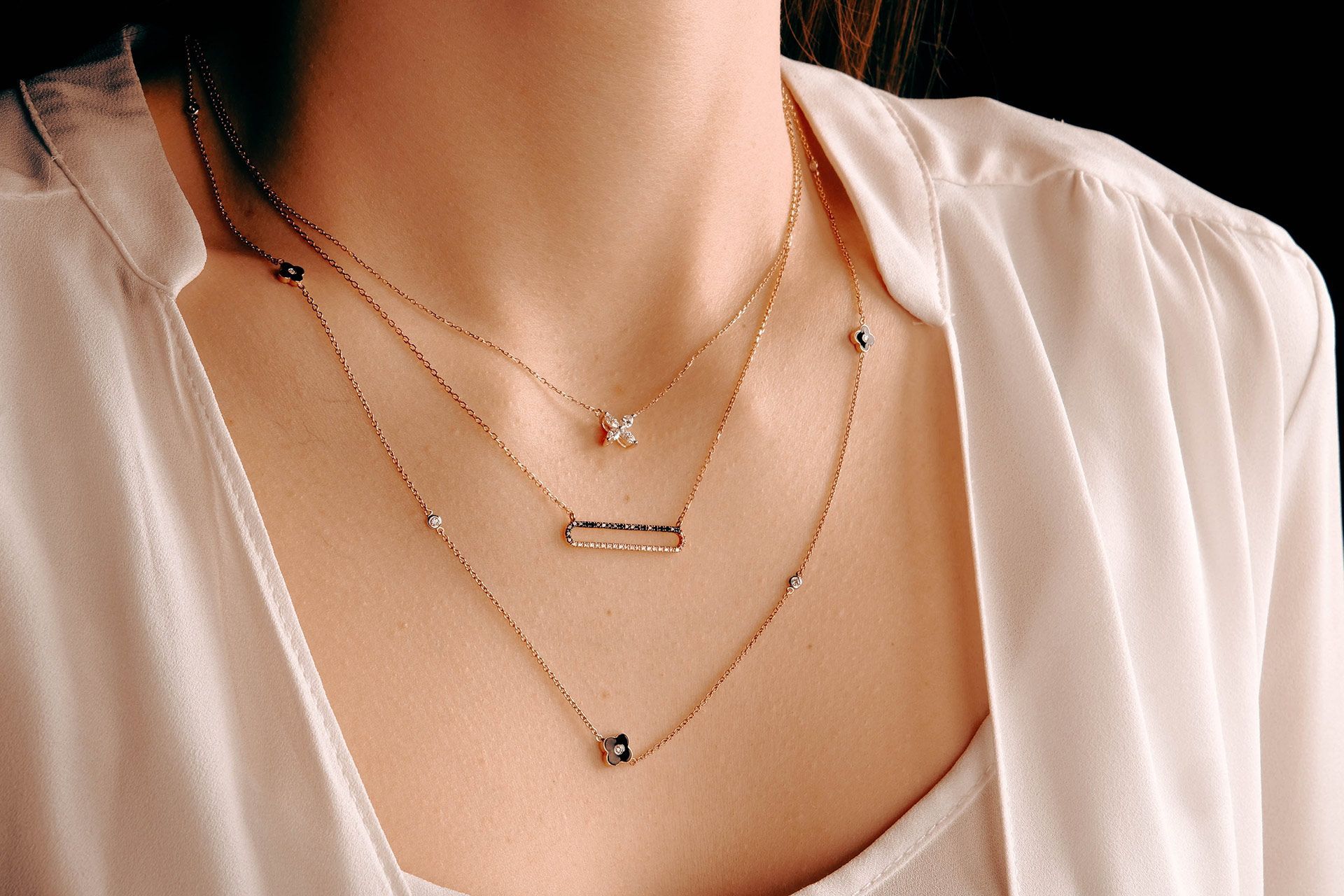Layered gold necklaces over a beige blouse on a person’s neck and chest